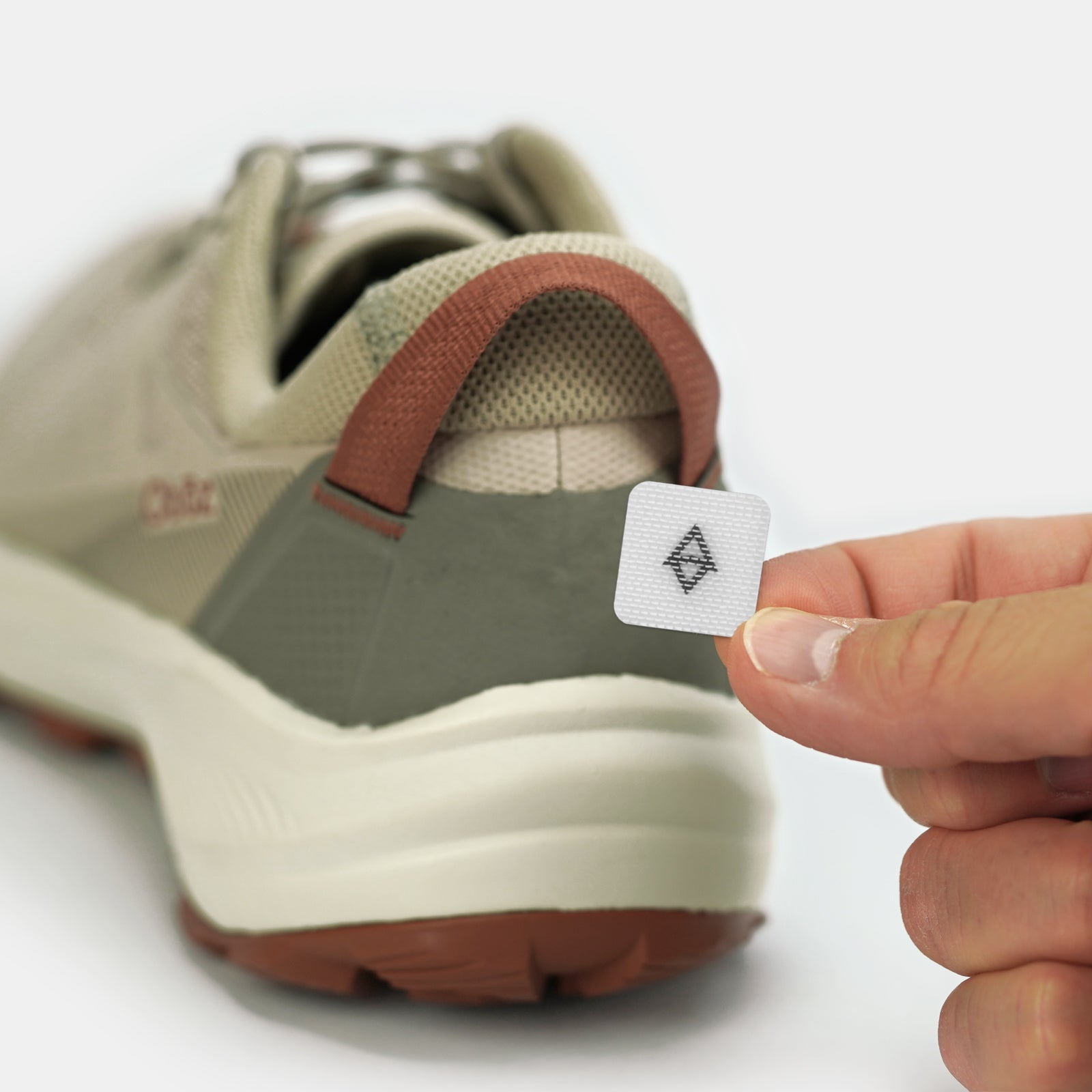 Person holding a white gaiter grip next to a shoe on a white background