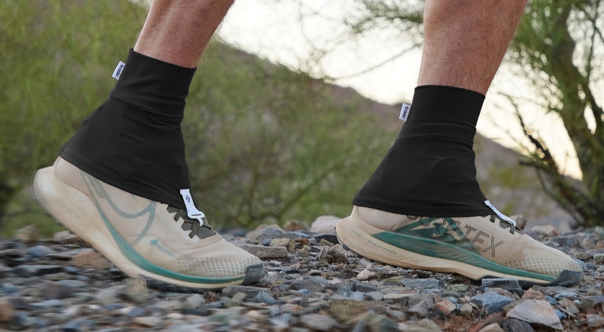 Person wearing running shoes with visible brand logos on a rocky trail.